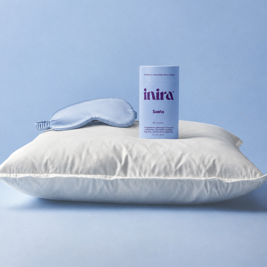 Bote de Inira Sueño sobre almohada blanca junto a antifaz azul, sobre fondo celeste